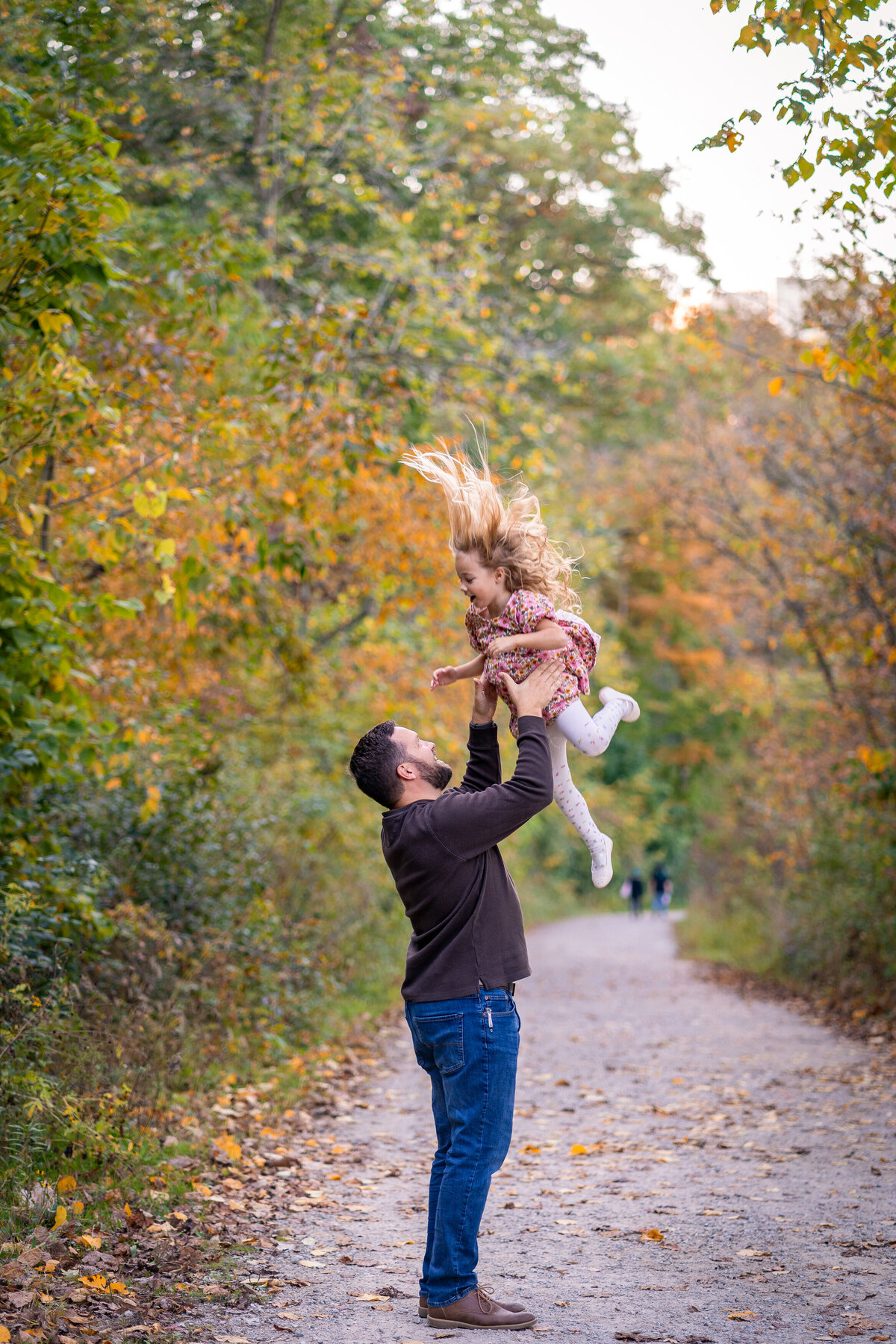 dad tossing daughter up in air while standing on a gravel path on a fall day 