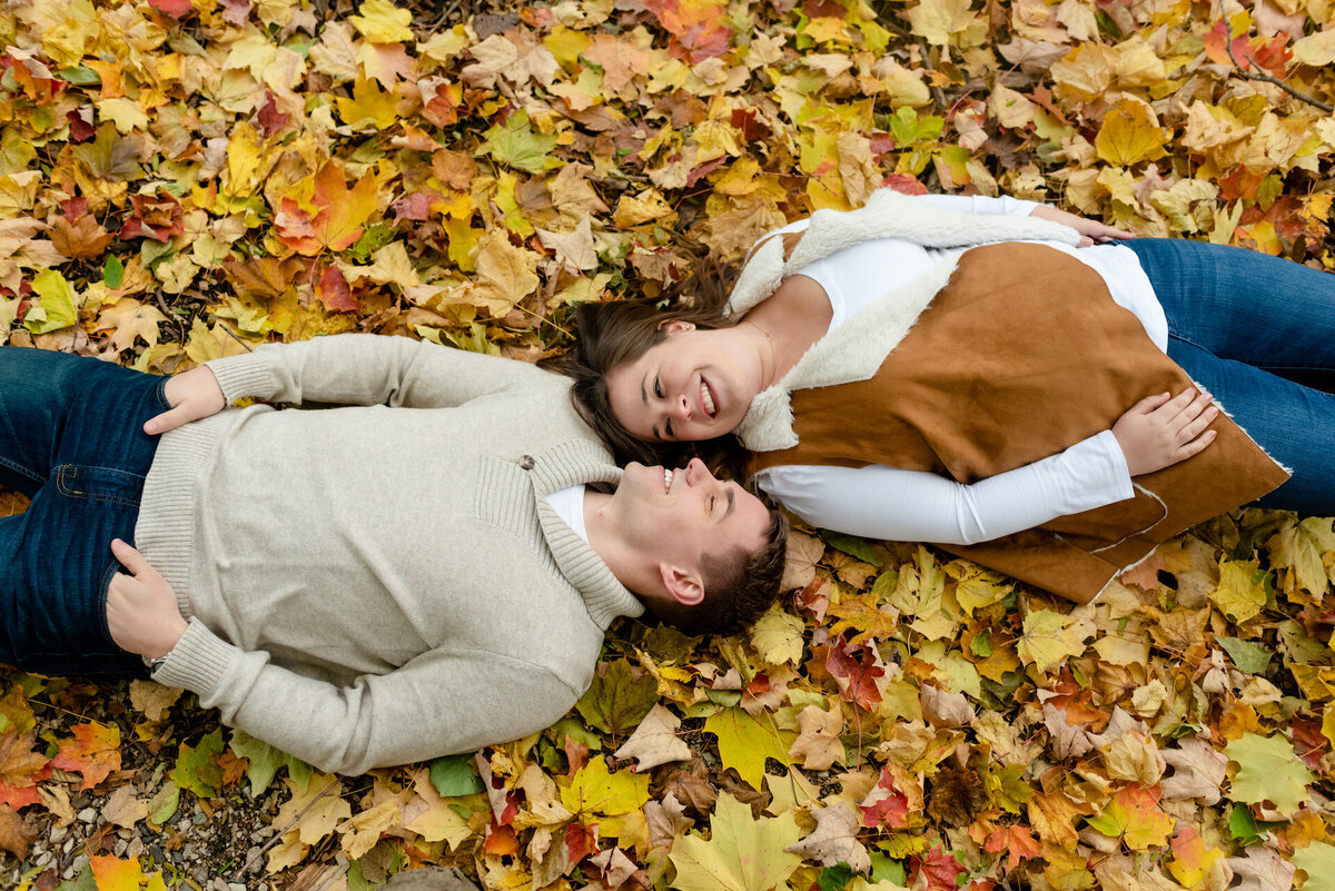 A couple lay on a pile of fall leaves