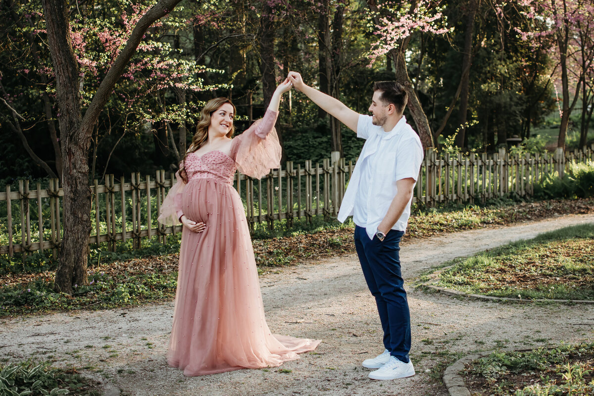 A pregnant mom in a beautiful blush maternity gown dancing with her hubby during a maternity photo session in Fabyan Japanese gardens,  Batavia IL