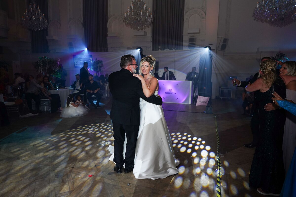 The bride shares a heartfelt dance with her father at the wedding reception. The image captures the tender moment between them, highlighting their special bond and the joy of the celebration. The scene is filled with warmth and emotion as they enjoy their dance together.