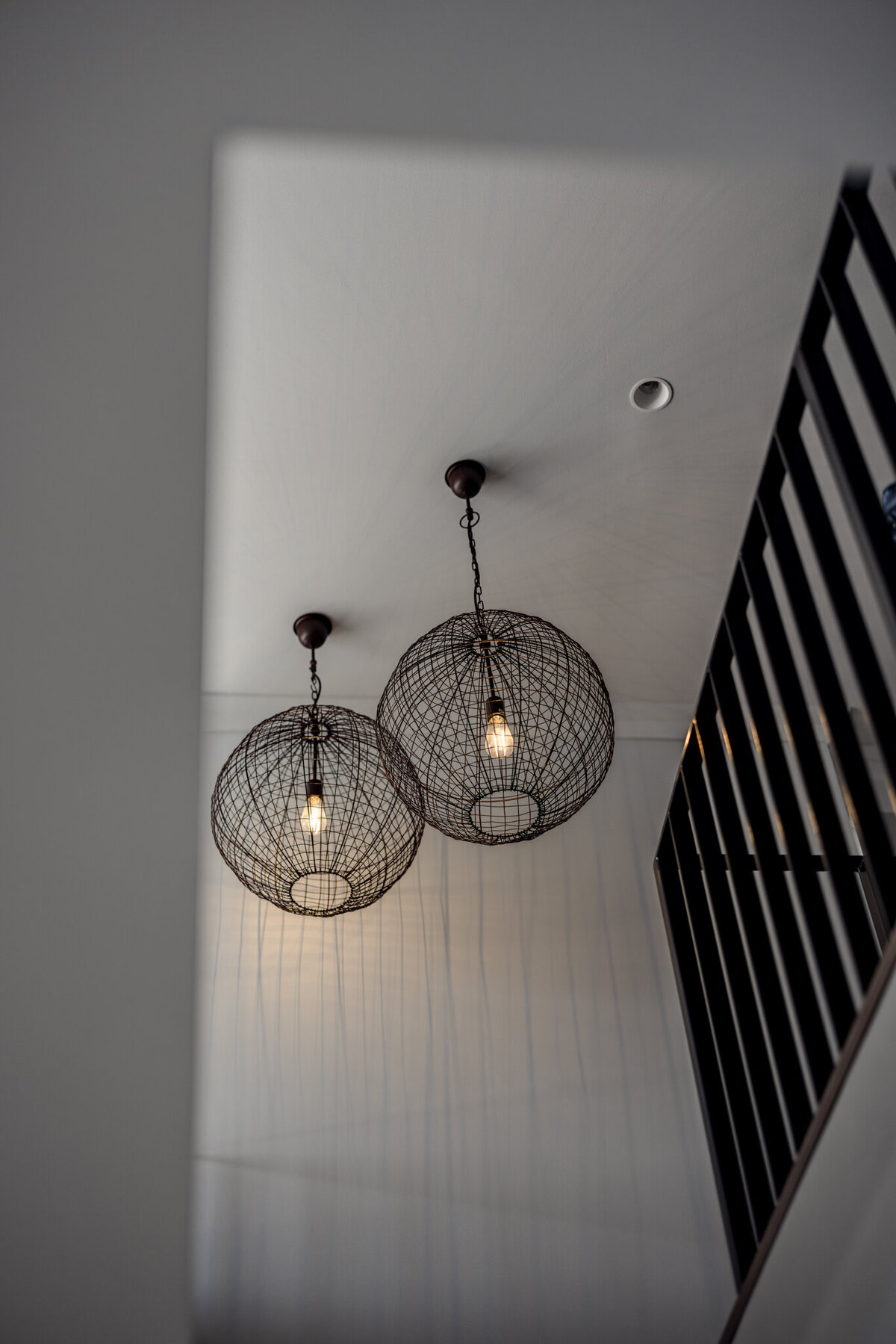 Two spherical wire pendant lights hang from the ceiling, casting shadows on the walls near a staircase railing. This exquisite touch reflects the expertise of a Newcastle interior designer, embodying bespoke interior design that transforms spaces in Newcastle, NSW.