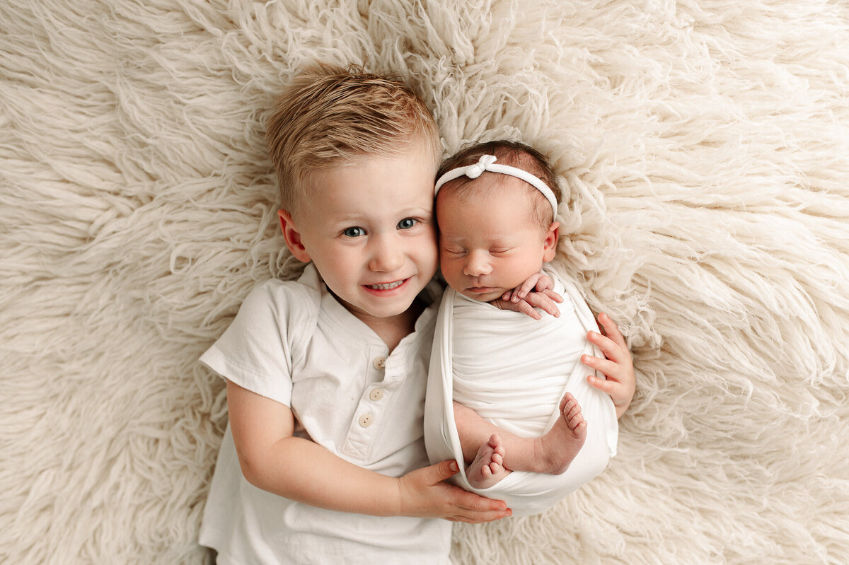 Brother holding newborn in ivory clothes luxury newborn session