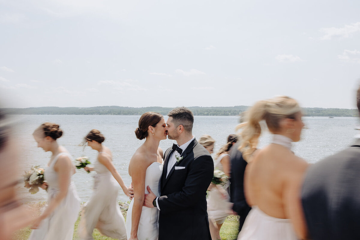 Bride and groom kissing as bridal party move behind them blurred out.