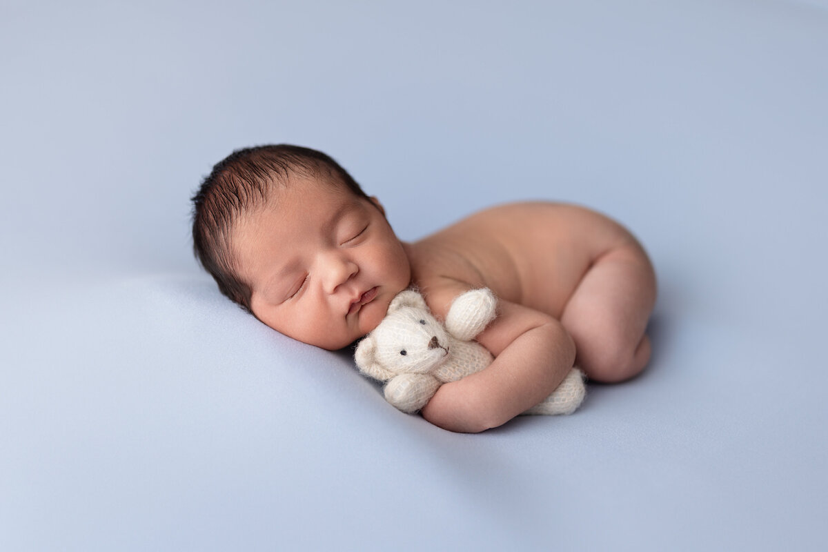 Newborn boy posed on his tummy holding a tiny felt teddy bear