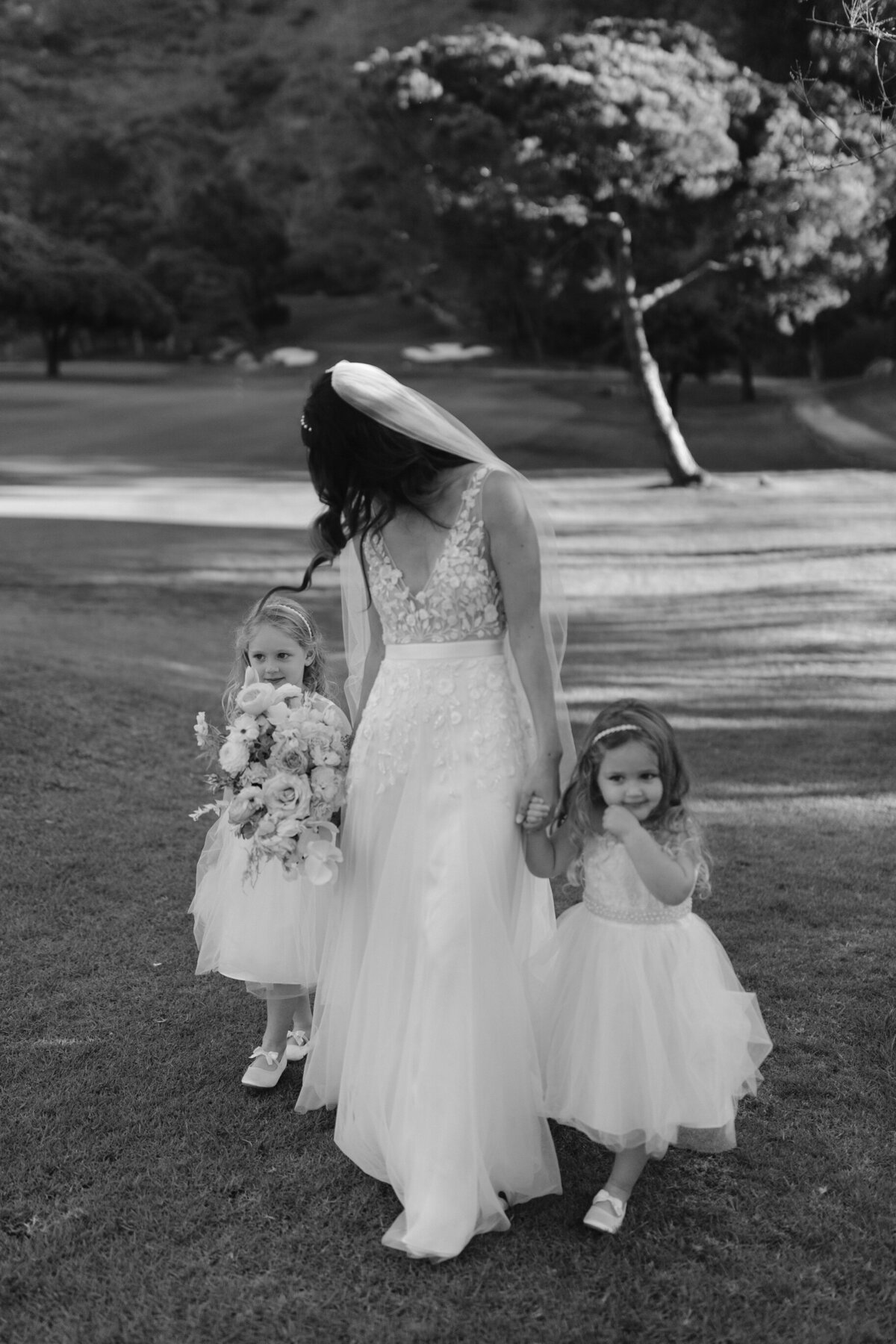 Bride in wedding dress walking towards the camera and holding hands with her flower girls