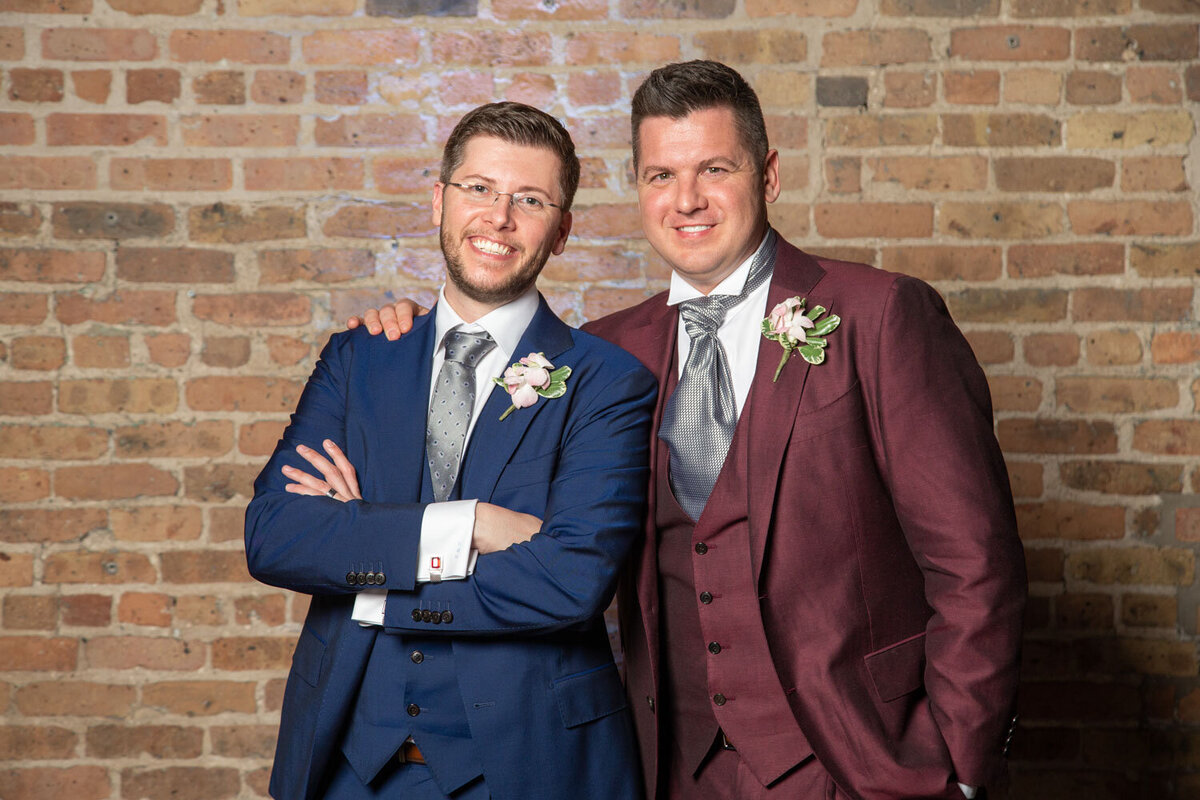 Two men in suits are posing for a picture in front of a brick wall