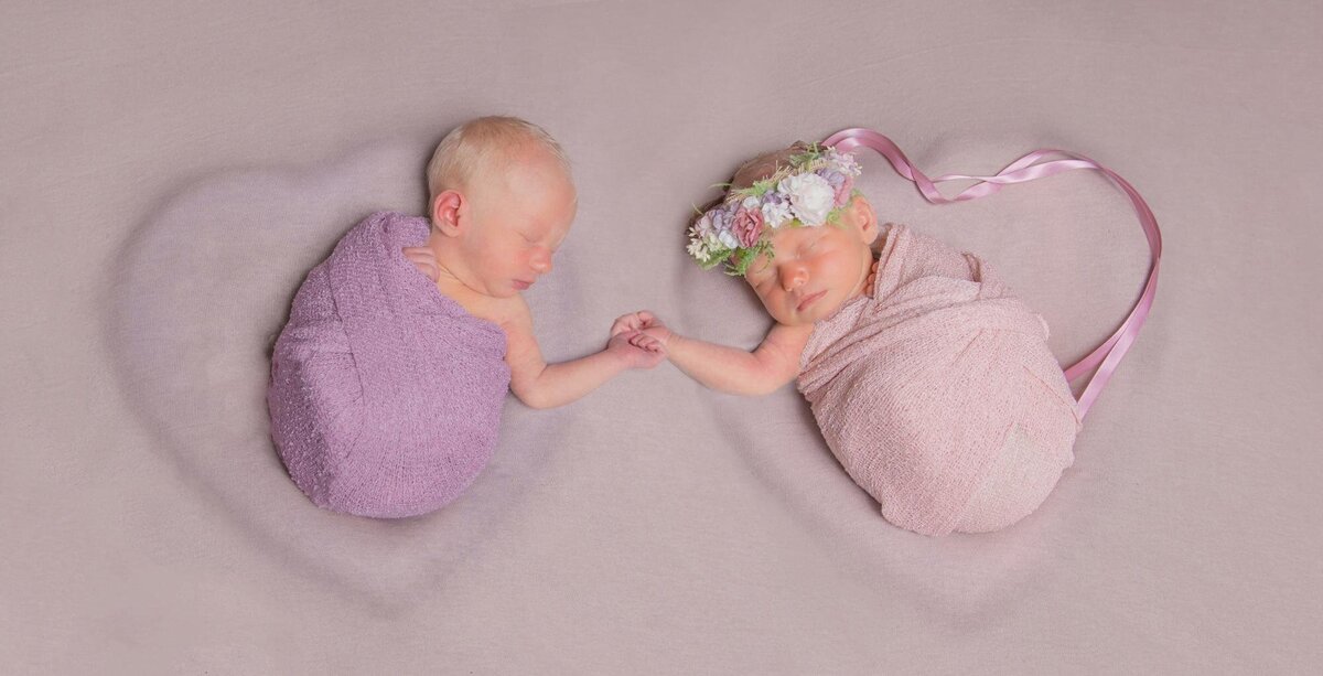 Twin babies holding hands in heart bowls