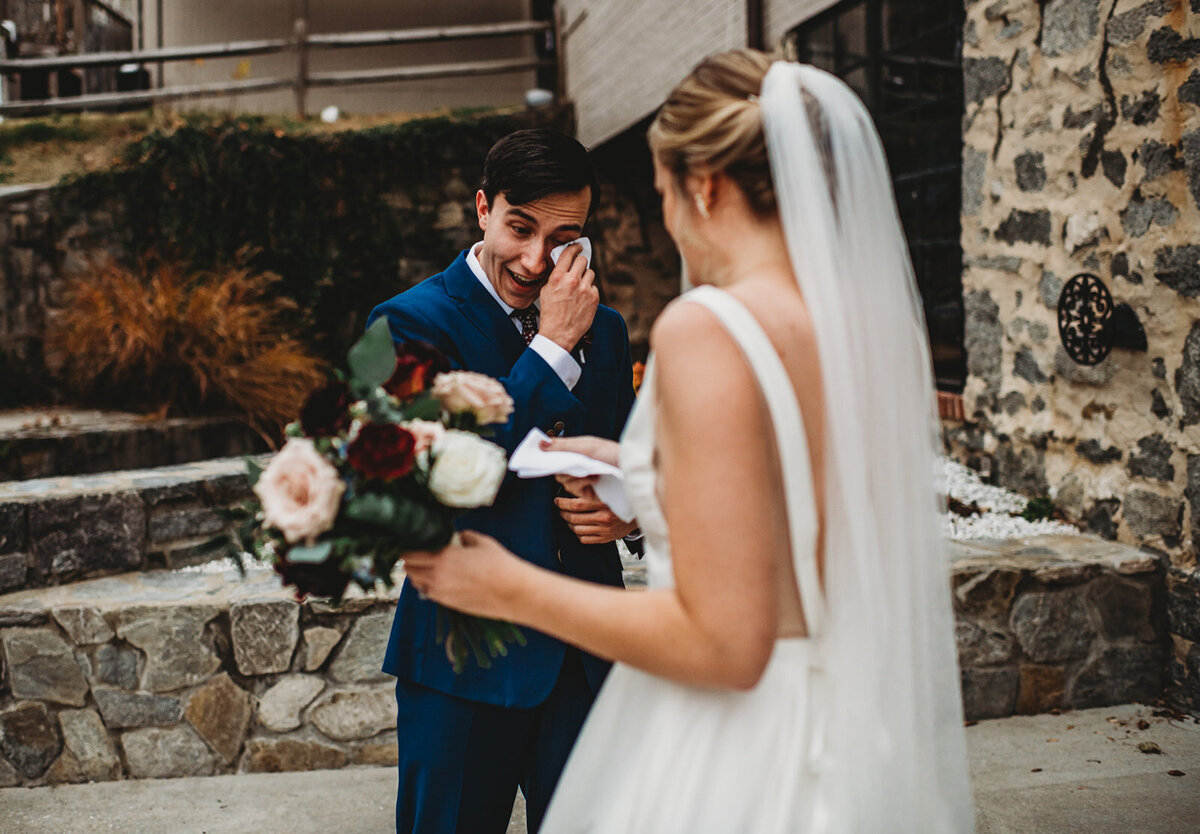 Bride and groom having their first look together outside of a stone wedding venue in Baltimore with groom wiping away tears and bride holding her wedding bouquet captured by Marilyn wedding photographer
