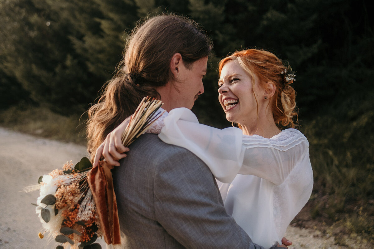 Holding each other in an embrace, bride and groom laugh heartly.