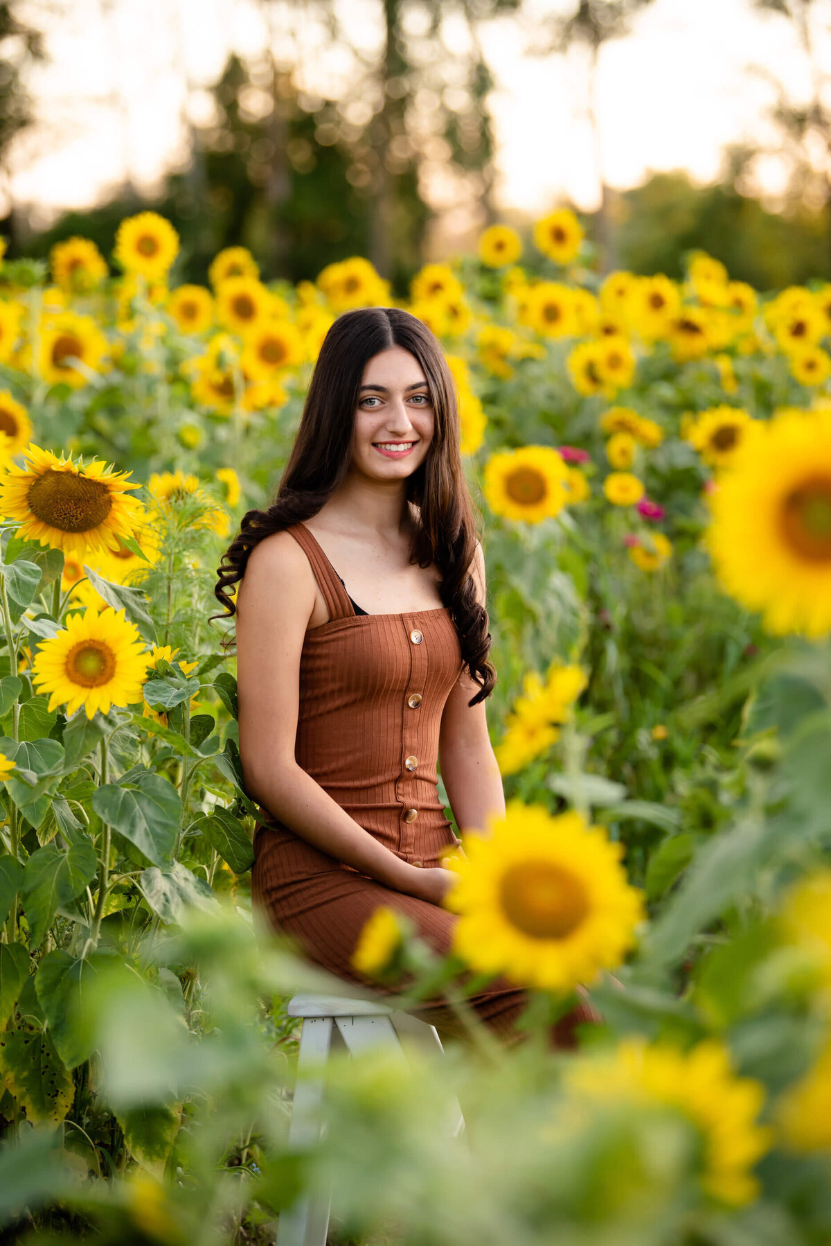 Teenage girl wearing burnt orange standing in a sunflower field for her summer Burlington family photography session