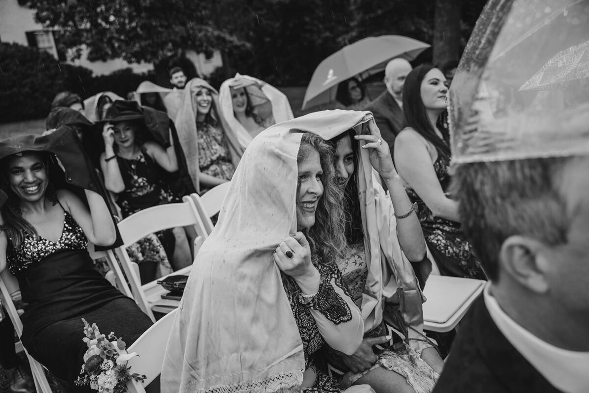 Wedding guests with scarves and umbrellas over their heads at a wedding ceremony 