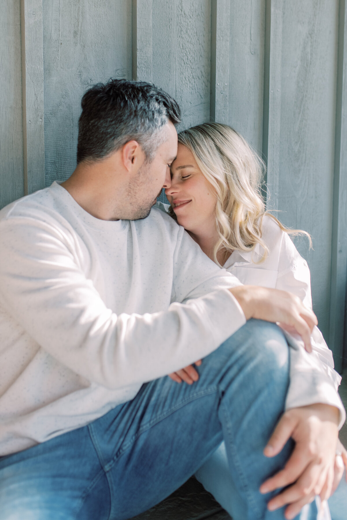 A couple shares a gentle kiss, bathed in soft morning light, barefoot on a rustic porch, sipping coffee in cozy comfort