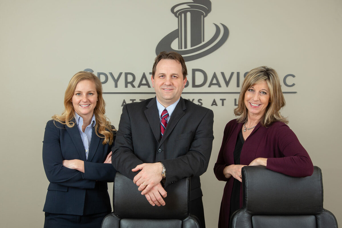 Three professionals posing in a law office with arms crossed