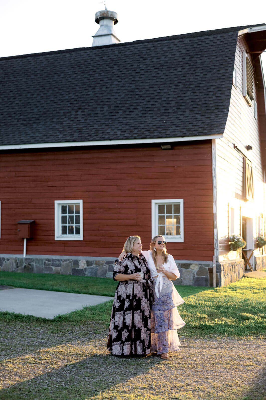 Two women in fashionable dresses are outside a big red barn at Lion Rock Farms, CT. Image by Jenny Fu Studio