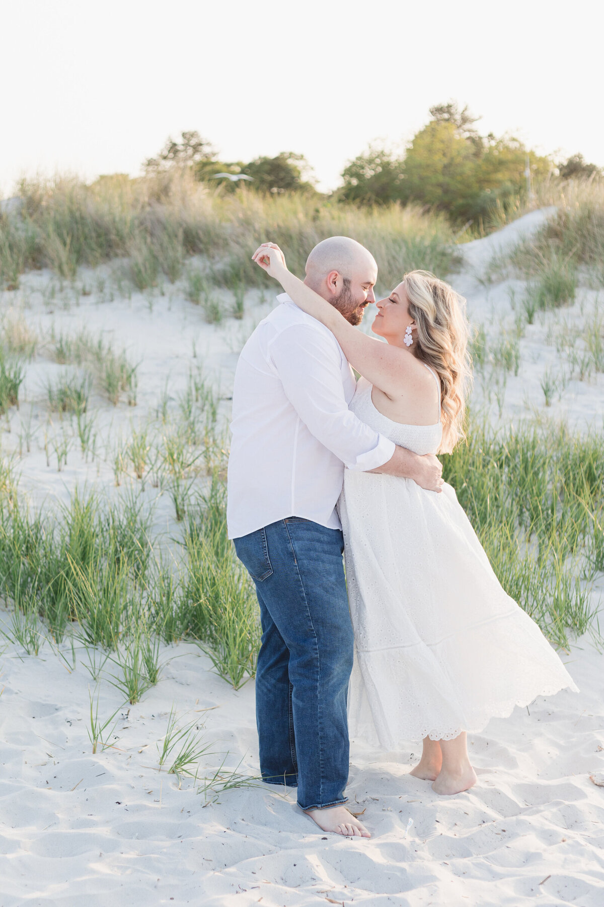 And engaged couple goes in for a kiss with sand dunes in the background