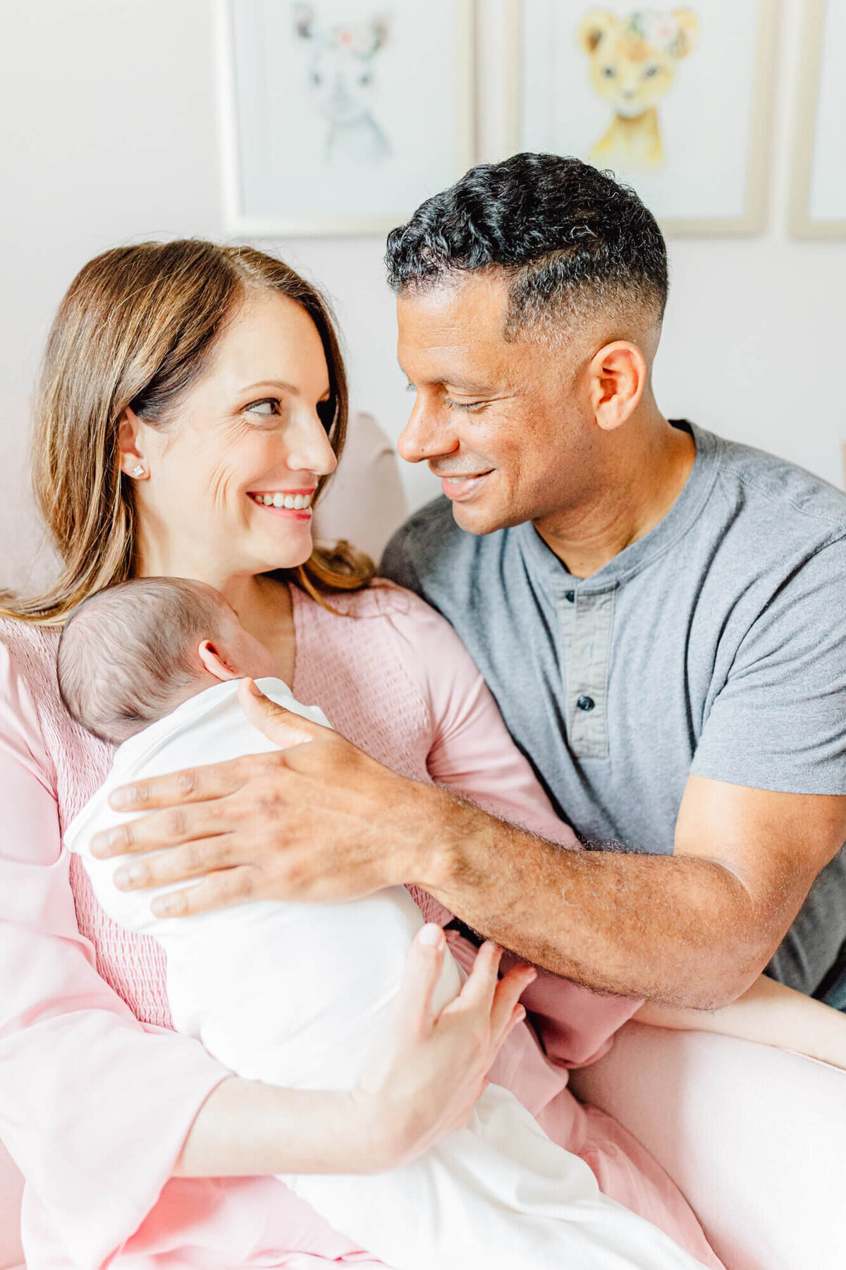 A mom holds her newborn in a chair in the nursery while dad smiles at her and rubs the baby's back