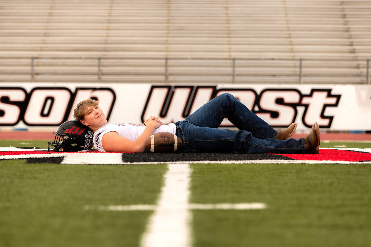 boy laying on helmet at 50 yard line with football jersey
