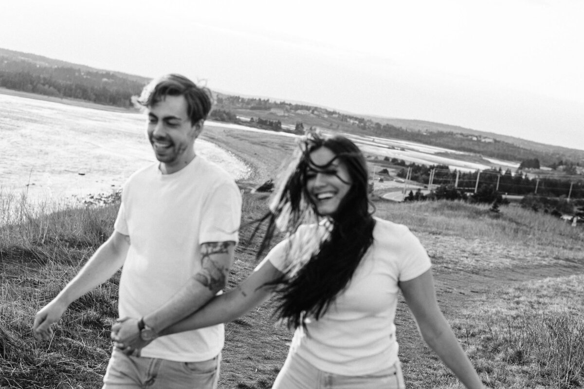 Happy couple holding hands while walking through beautiful Nova Scotia landscape.