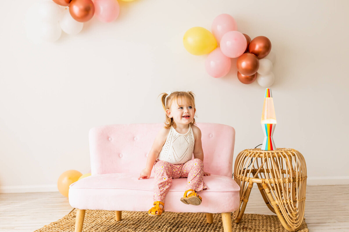 Toddler girl dresses in bell bottoms and a lace romper sitting on a pink couch