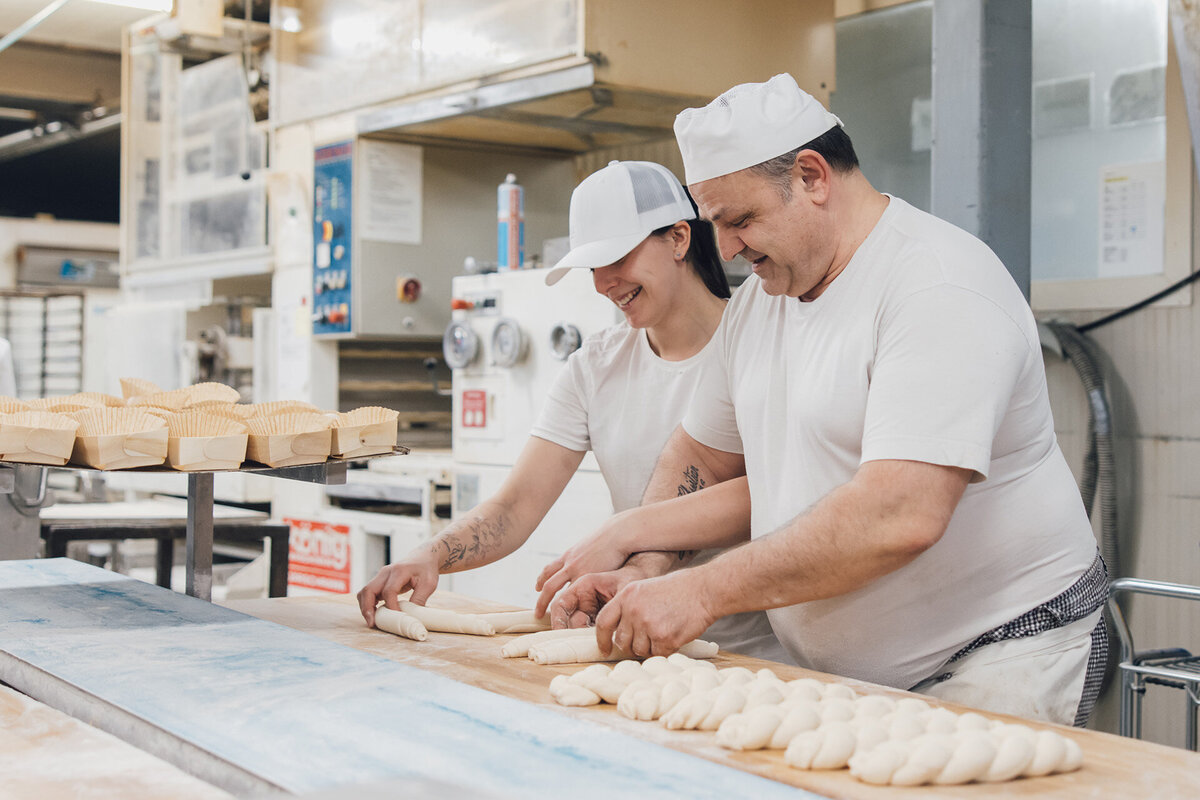 Bäcker und Bäckerin formen gemeinsam einen Dinkelzopf