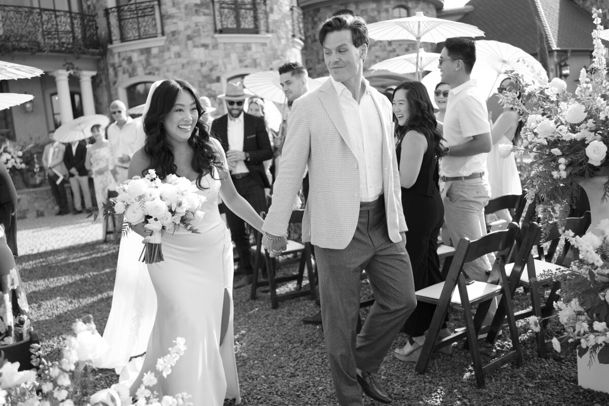 black and white photo of wedding couple holding hands walking down aisle