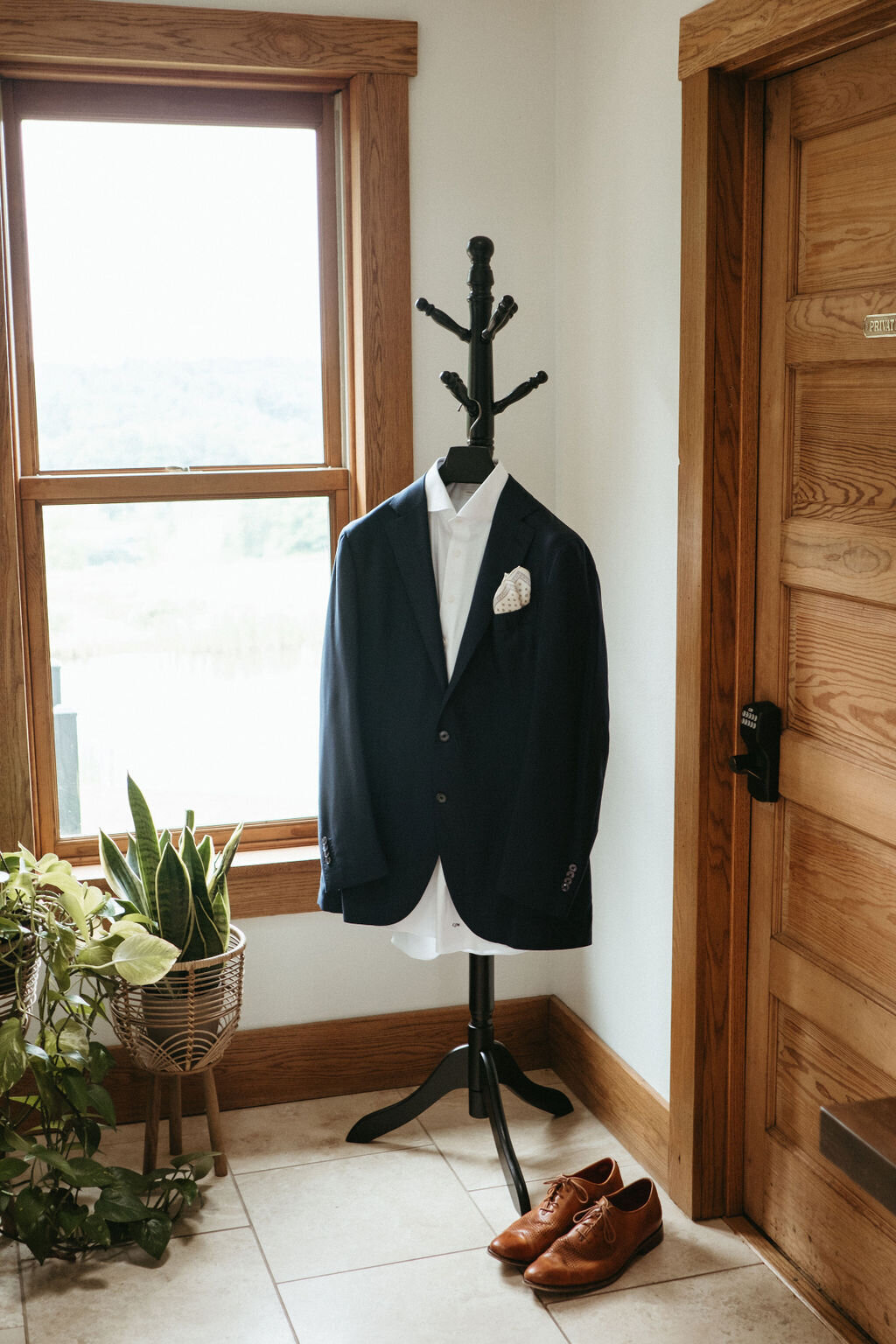 a groom's suit and dress shoes in the entry hallway on a coat stand in the modern farmhouse overnight accommodations at Willowbrook wedding venue