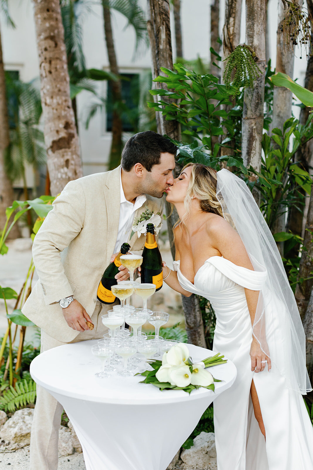 Monica and Austyn kiss in front of a champagne tower, capturing a joyful moment at their tropical Florida Keys wedding reception.