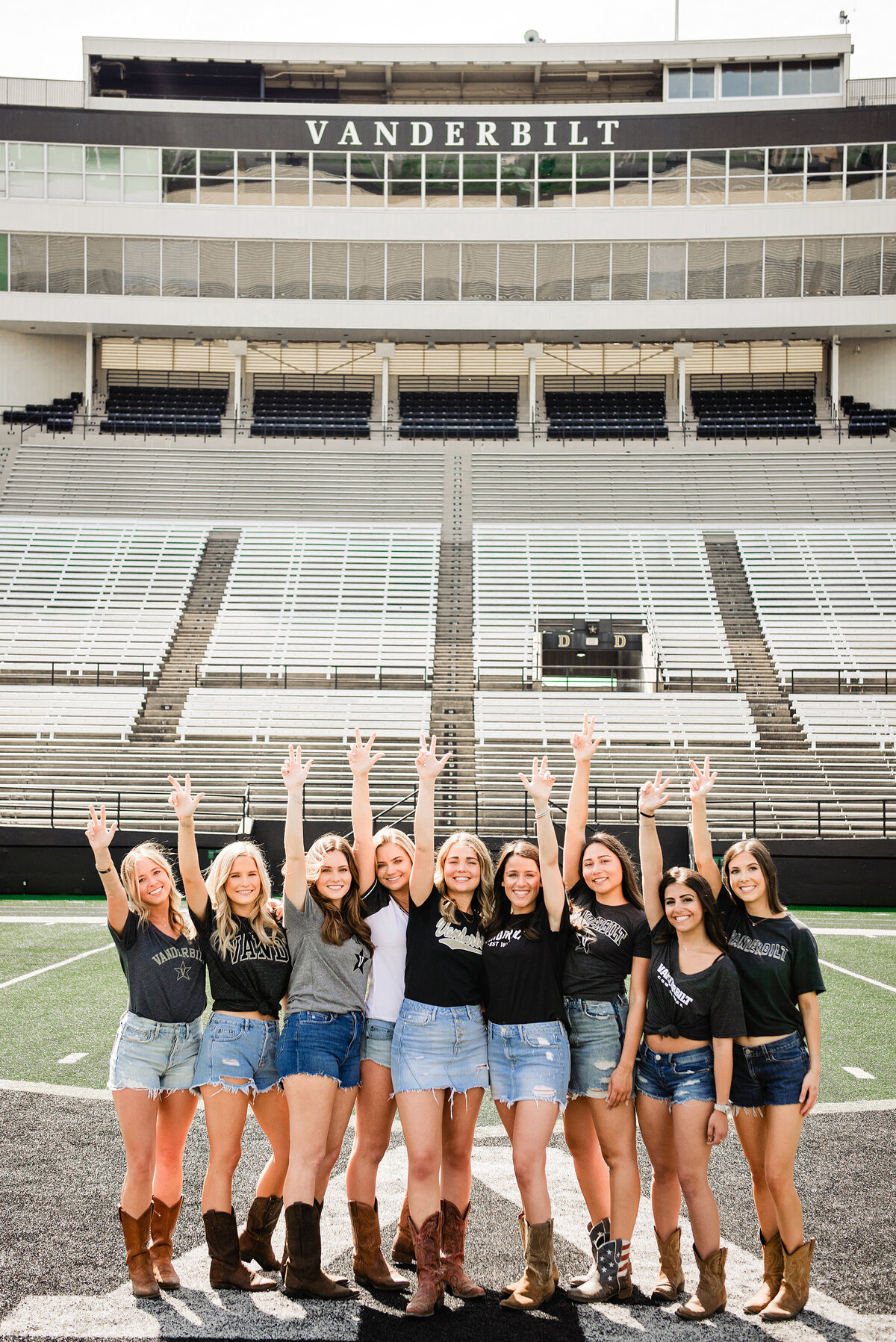 Group of senior girls wearing college shirts and jean skirts standing on football field throwing Vanderbilt anchor down hand sign over heads
