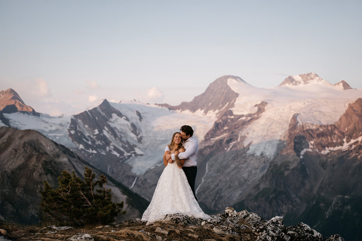 Bride and groom embrace as the sun lights up the glacier behind during backcountry elopement