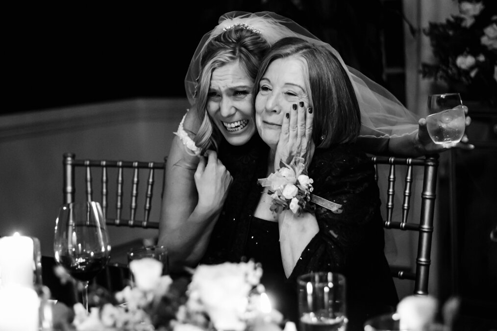 Two women hugging at a table at a wedding.