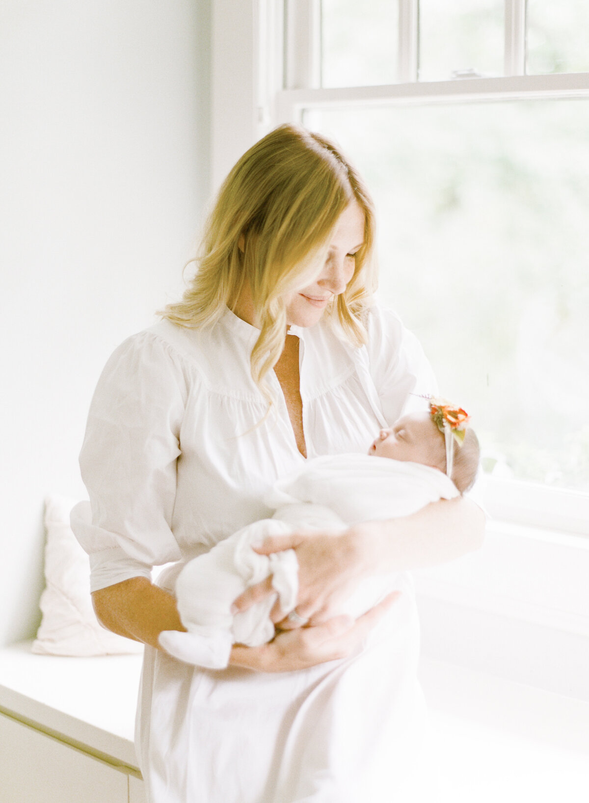 Mom sits and holds her newborn daughter in bright window light during their Raleigh newborn photography session. Photographed by Raleigh Newborn Photographer A.J. Dunlap Photography.