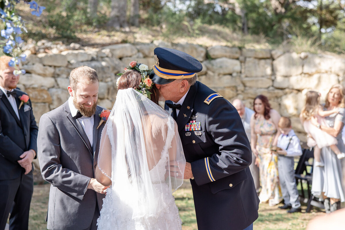 father of the bride kisses her at the alter while wearing military uniform at Hayes Hollow at Hidden Falls in Spring Branch Texas