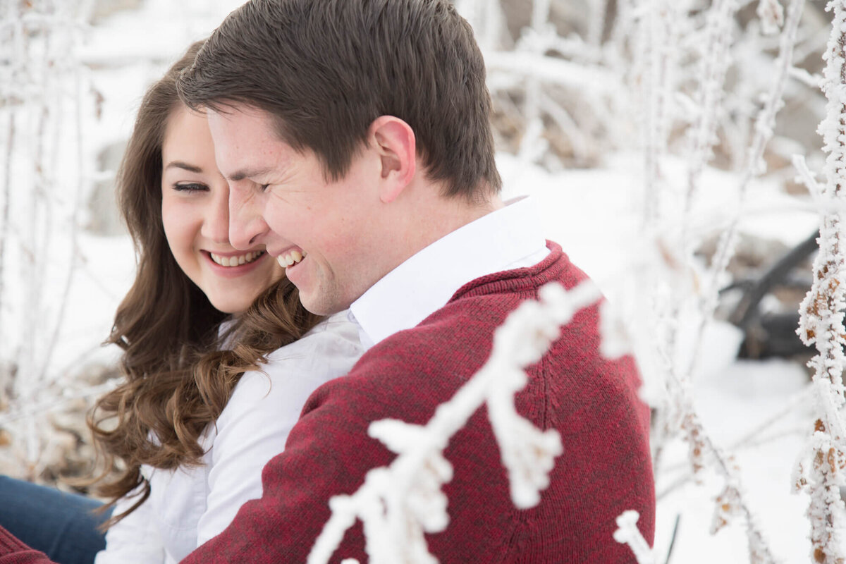 a couple laughing by a frosted bush, enjoying their engagement