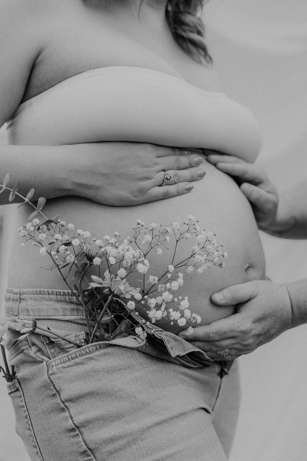 A pregnant woman holds her belly while holding flowers