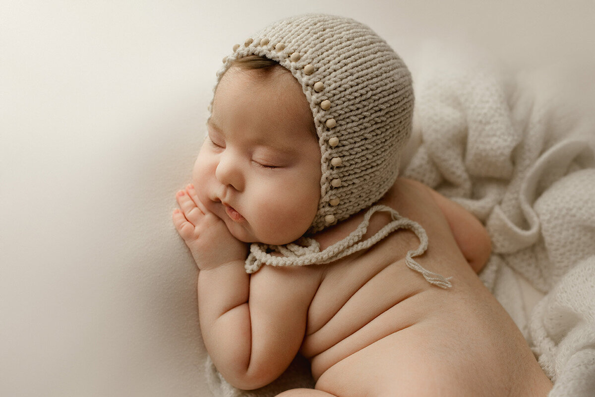 a newborn boy wearing a beaded bonnet lays on his tummy with his hand under his cheek