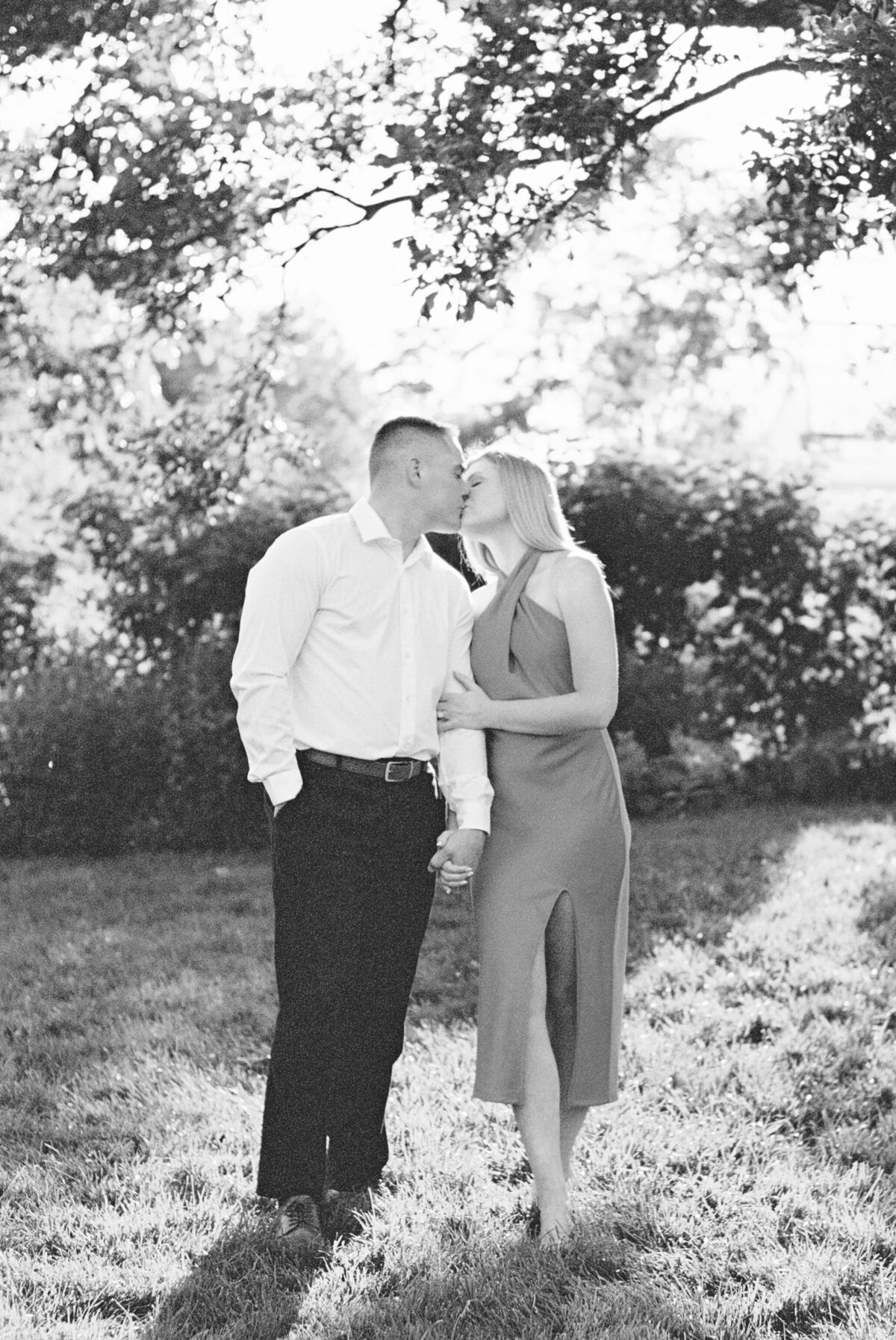 Black and white photo of engaged couple kisses surrounded by lush Columbus garden shot by Philadelphia photographer.