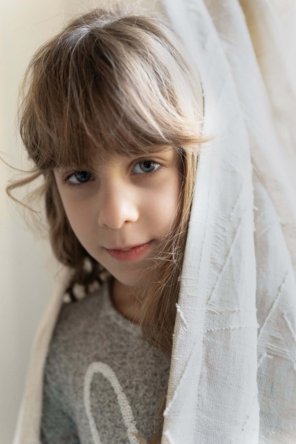 young girl peeks out from behind curtain