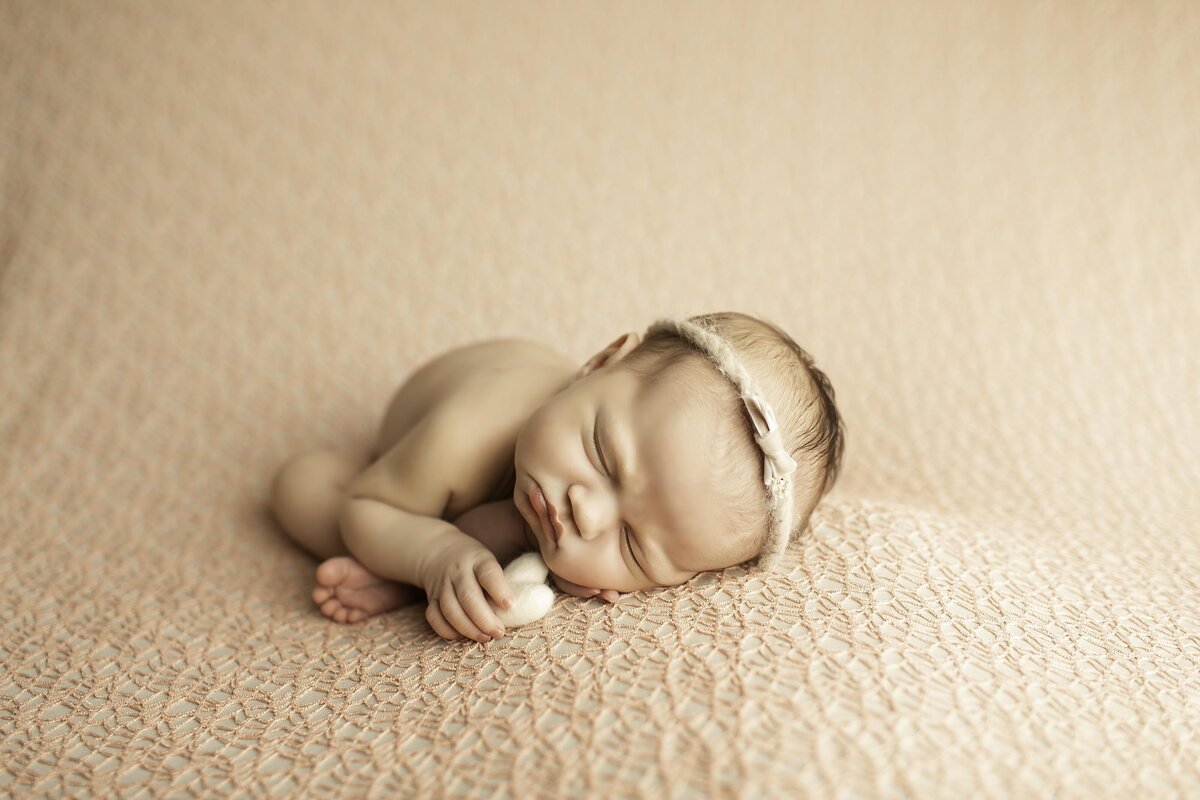 Newborn baby girl peacefully sleeping while gently holding a small heart prop in her tiny hands, creating a sweet and loving scene
