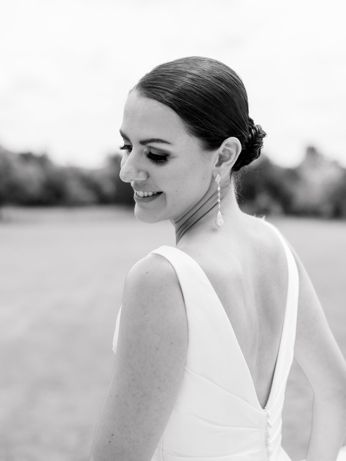 Black and white bridal portrait at Cairnwood Estate by Philadelphia Fine Art Wedding Photographer Elizabeth Kane, featuring a close-up of a bride in a sleek V-back wedding gown and elegant pearl drop earrings—capturing timeless beauty and classic East Coast wedding style.