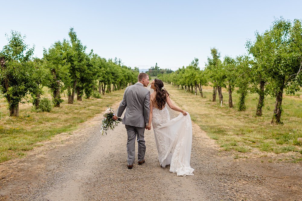 Bride and groom walking hand in hand in pear orchard