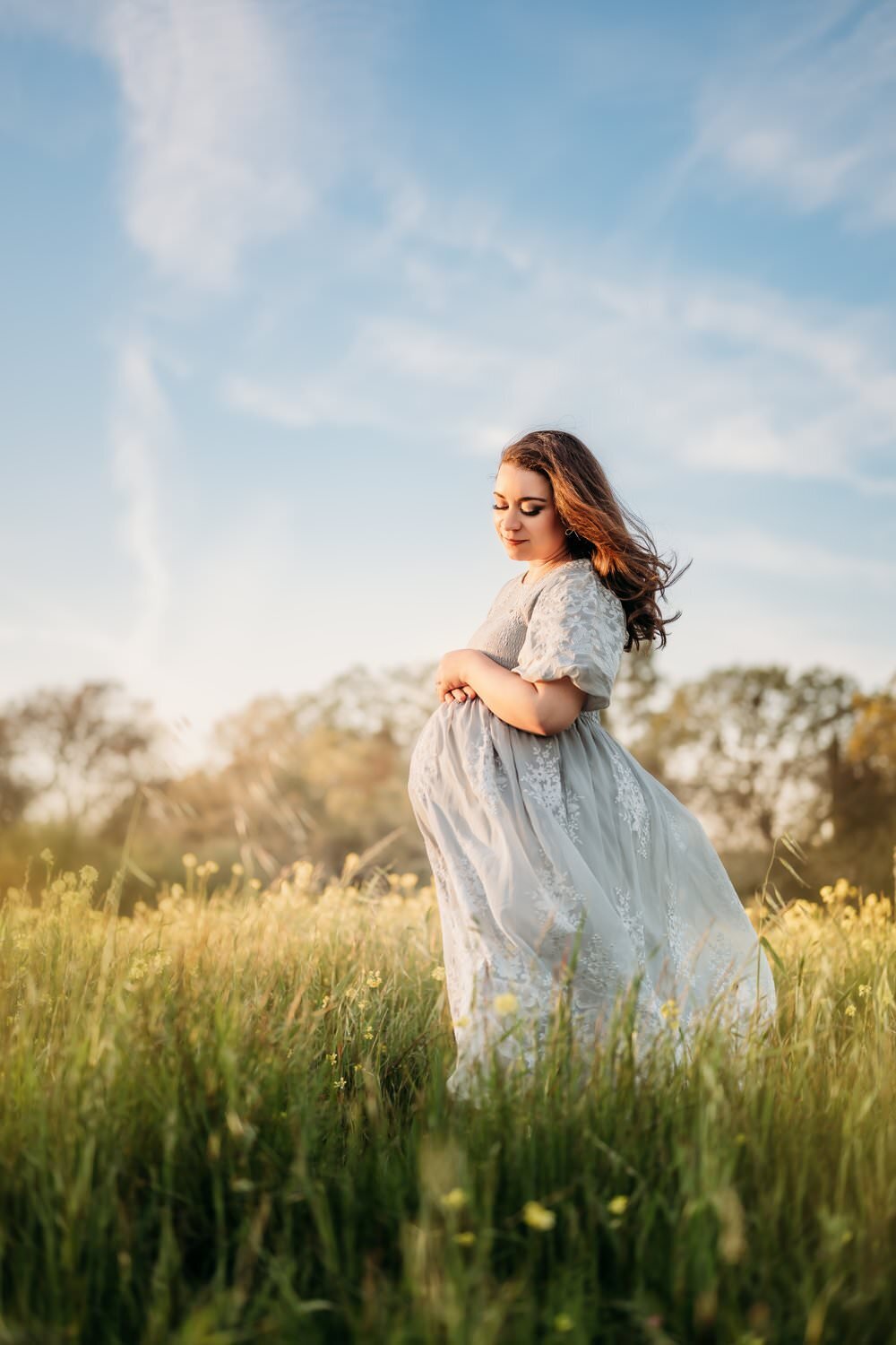 maternity photo of mama in a field of yellow wildflowers. she softly looks down at her belly