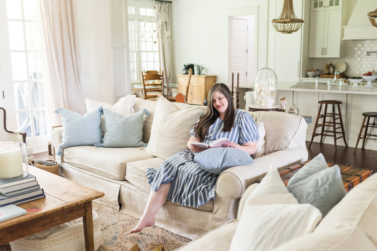Lauren sits on her family room sofa reading a book in blue and white striped dress