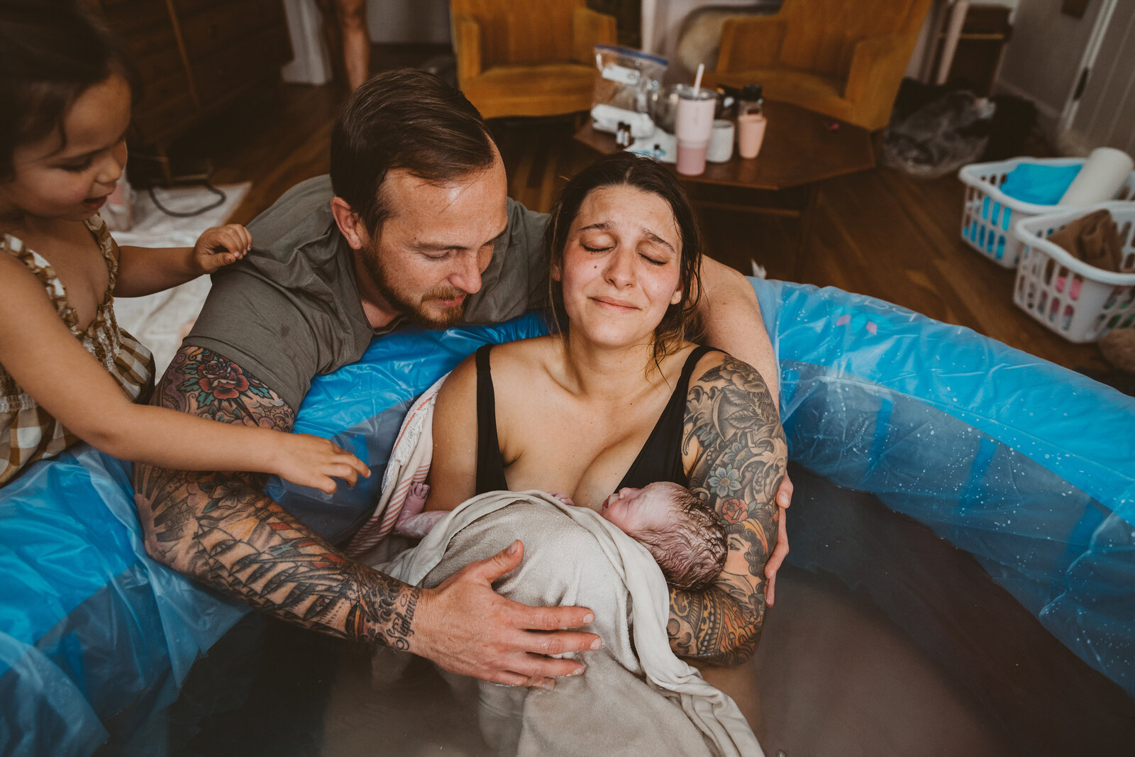 mom emotionally holding her new baby as dad and big sister reach for the baby too