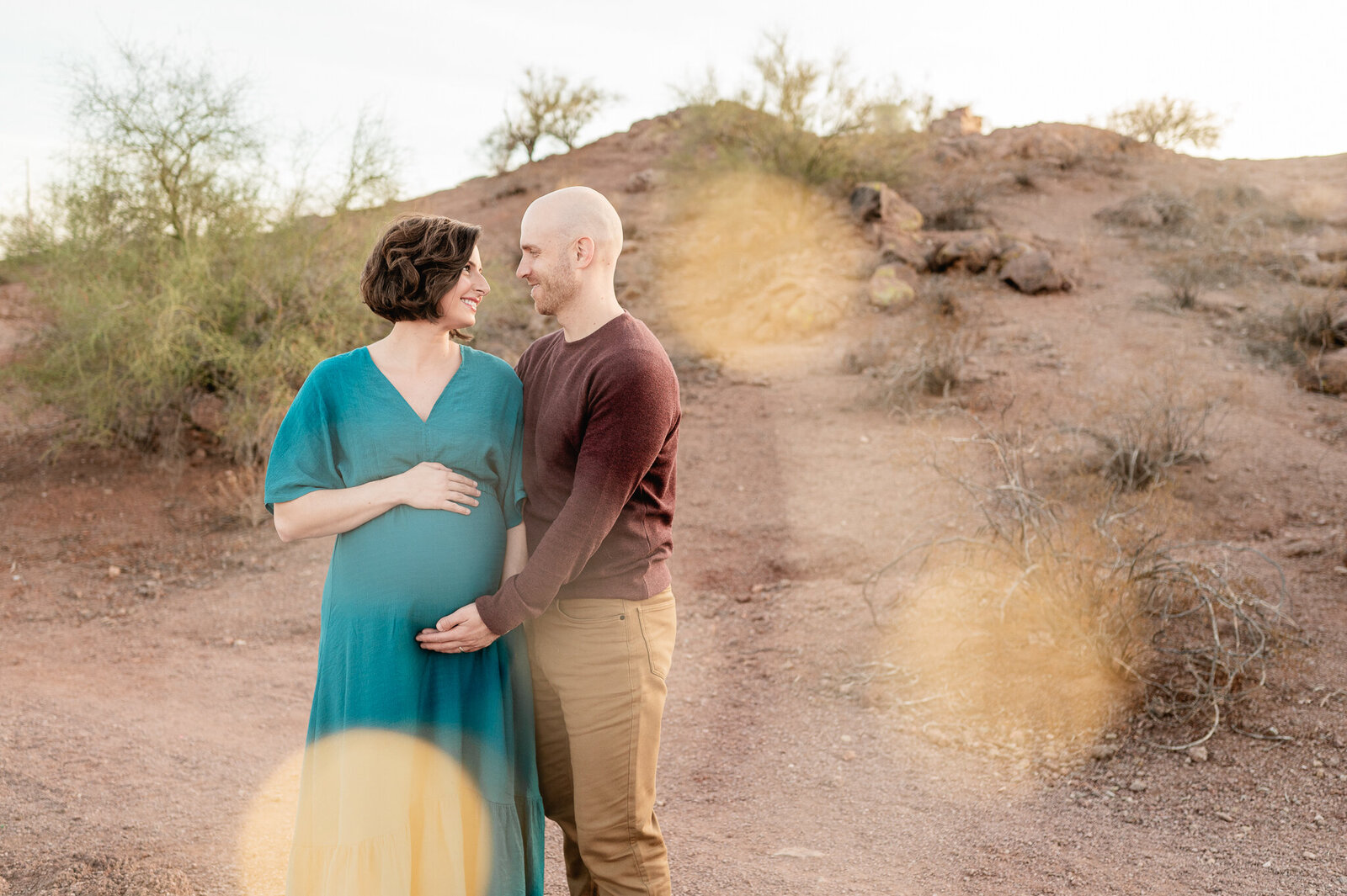 pregnant mom being held by her husband while they look at each other at sunset in front of the Phoenix desert backdrop
