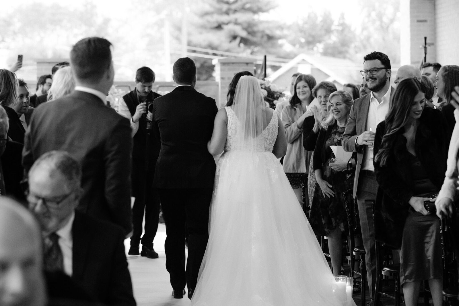 a bride walks down the aisle with a man in a suit surrounded by smiling guests