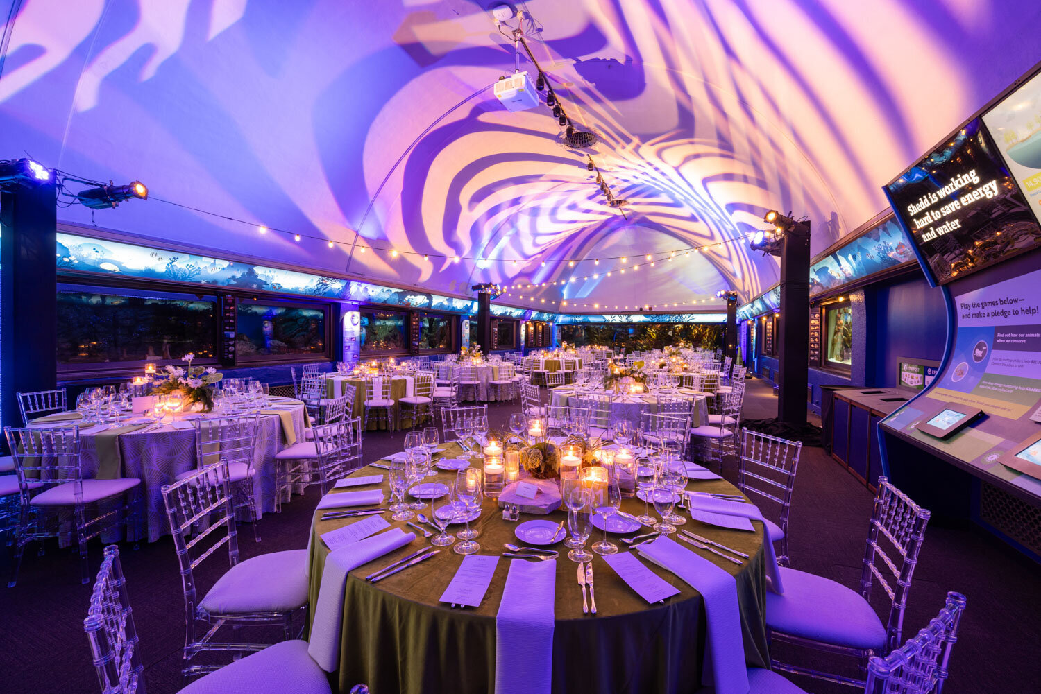 Candlelit round tables under a tent with purple lighting and draped ceiling
