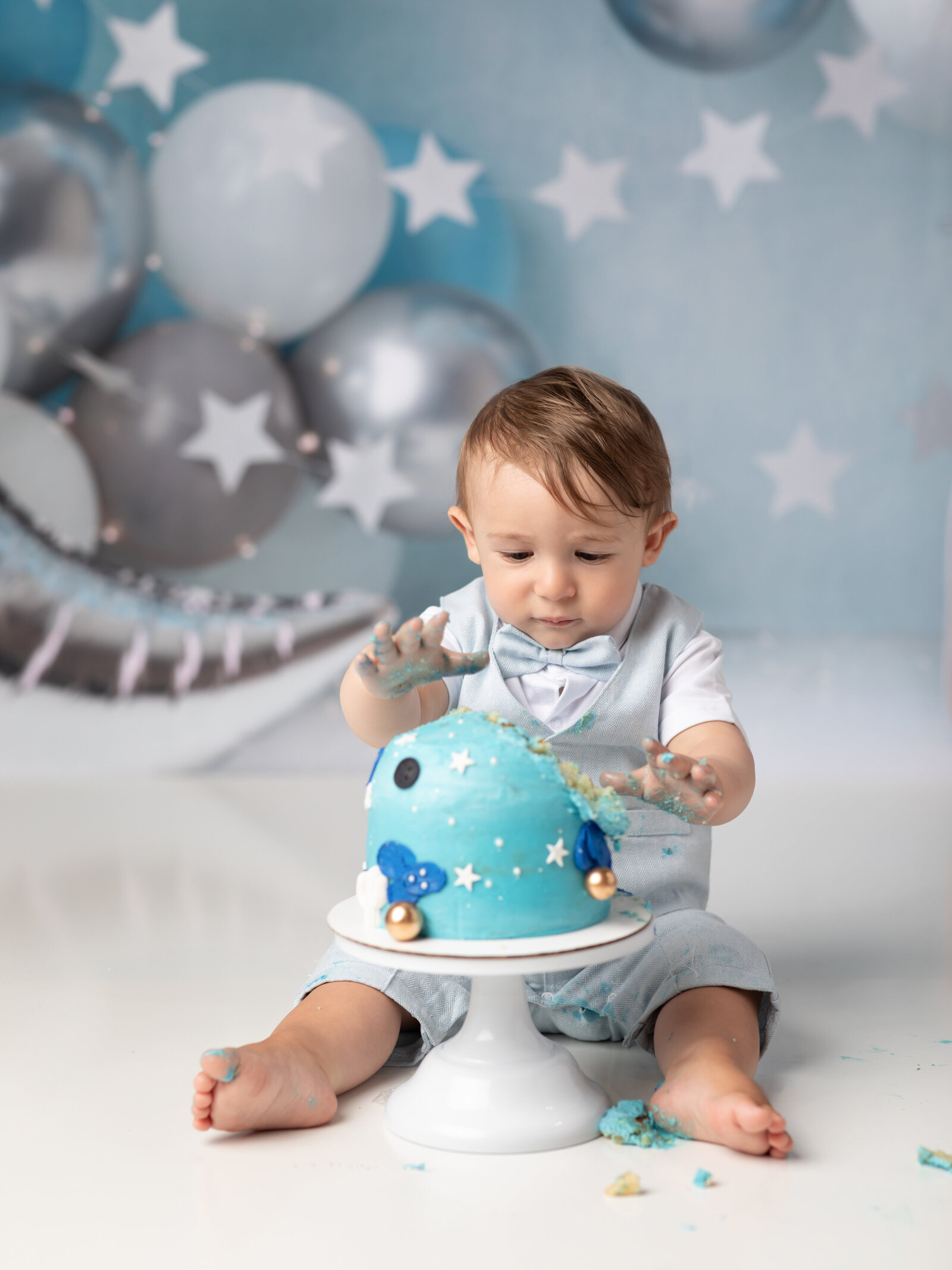 one year old boy grabbing for blue cake at a first birthday photoshoot