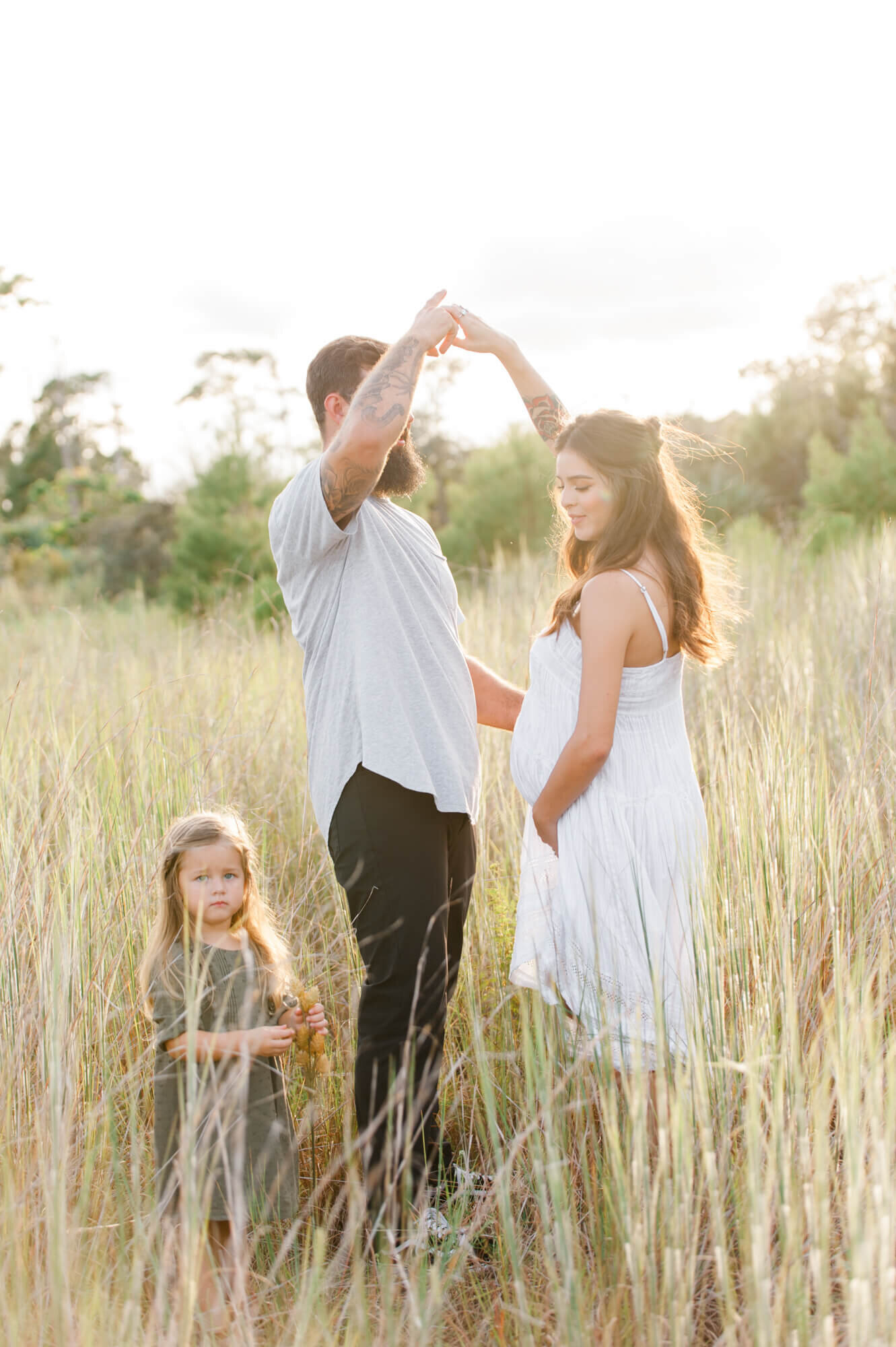 Dad gives mom a twirl while their family of three is standing in a  tall grass field