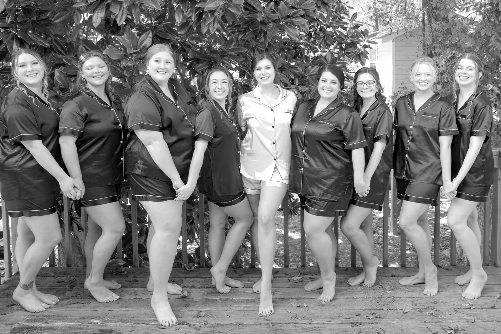 The bride and her bridesmaids pose together in matching pajamas on a wooden deck surrounded by greenery, captured during a Boone, NC wedding, highlighting fun and authentic pre-ceremony moments.