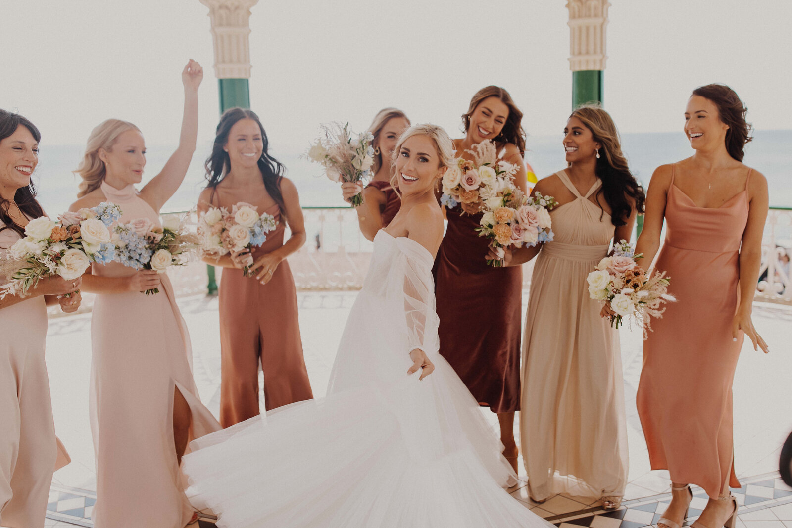 A Bride surrounded by her bridesmaids each holding their bridesmaid bouquets celebrating and smiling at their West Sussex wedding venue